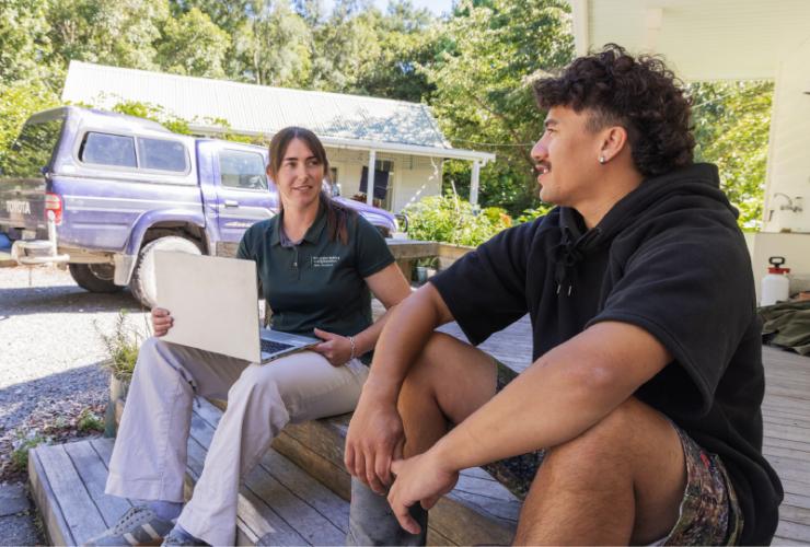 Two people talking, sitting on a wooden porch.