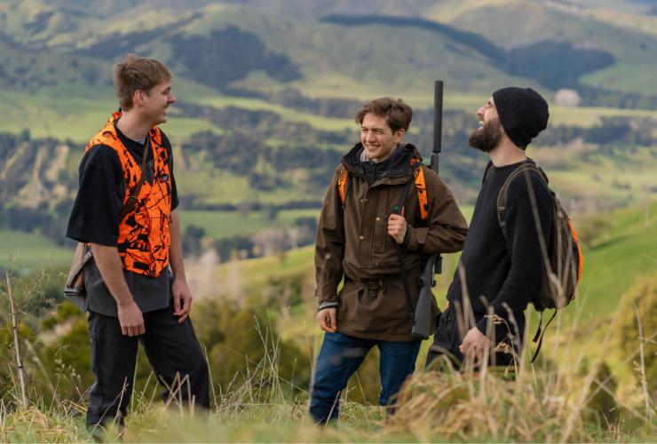 3 young hunters laugh together on the side of a hill in the countryside